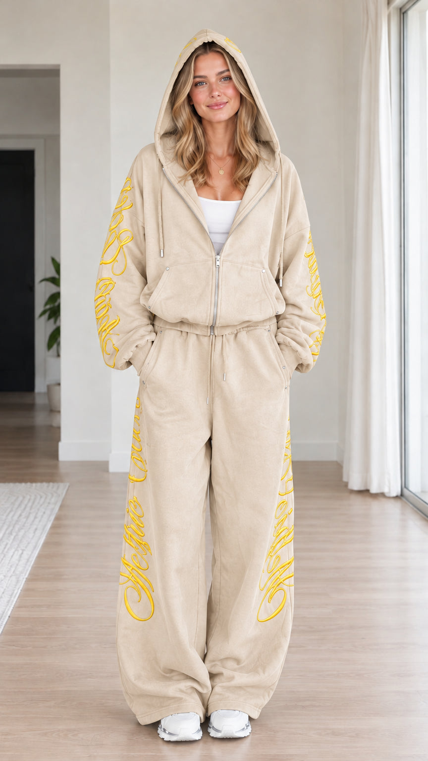 Front view of woman wearing beige oatmeal script embroidered zip-up hoodie and wide-leg sweatpants set